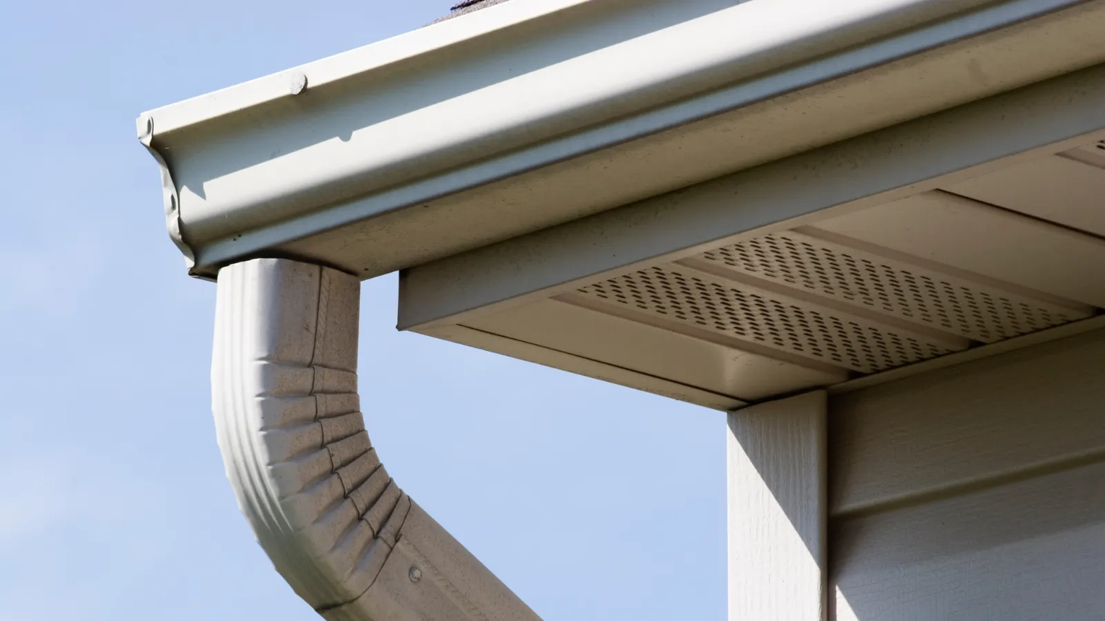 Corner with vented soffit showing a white gutter and downspout
